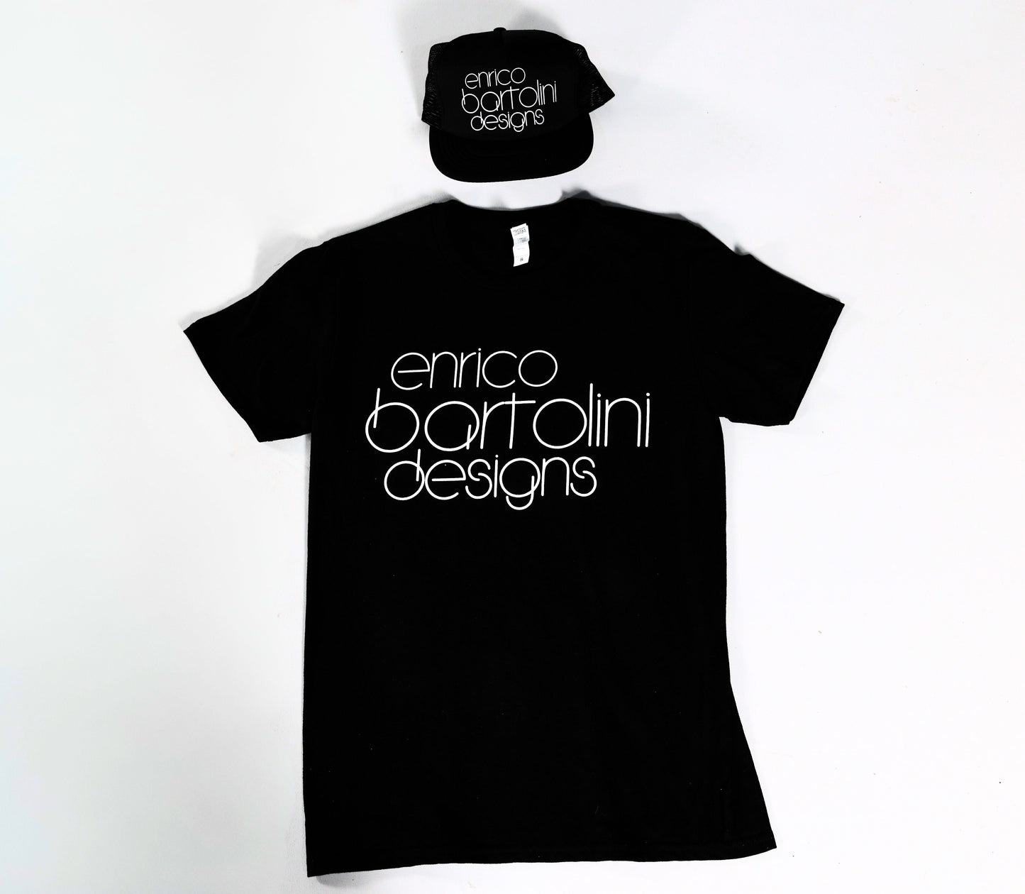 Black t-shirt and cap with 'enrico bartolini designs' text on a white background