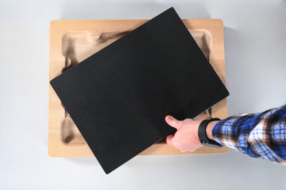 Person placing a black cutting board insert on a wooden cutting board with a white background