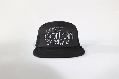 Black cap with 'enrico bartolini designs' text on a white background